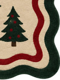 A rectangular holiday-themed rug with a scalloped border, featuring brown leaping reindeer with red scarves, dark green Christmas trees, gold stars, and red holly motifs on a beige background.