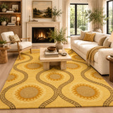 A large yellow area rug with a repeating sunflower and oval pattern in tan and brown, styled in a bright, modern living room with a white sofa, fireplace, and wooden coffee table.