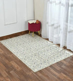 Gray and white geometric floral patterned rug on dark wood floor near red stool with open book and mug