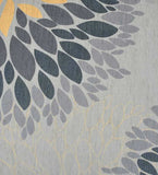 Close-up of a gray modern floral rug with layered petal patterns in yellow, dark blue, and light gray.