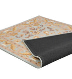 Light blue and beige traditional area rug with floral and vine patterns, folded corner showing black backing