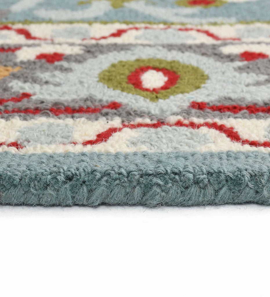 Close-up of a hand tufted traditional patterned rug with light blue, red, green, and blue colors.