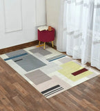 Modern Bauhaus geometric rug with blue, yellow, and red blocks on hardwood floor next to burgundy stool