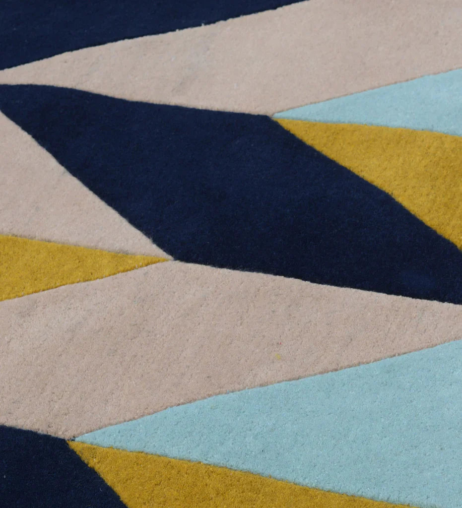 Modern hand-tufted geometric wool rug with bold chevron pattern in mustard yellow, navy blue, blush pink, and sky blue.