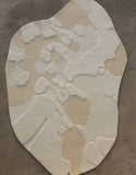 Irregular-shaped modern neutral rug with abstract organic beige and cream pattern on concrete floor