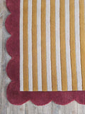 Striped rug with mustard and gray vertical stripes, scalloped deep red edge on wood floor
