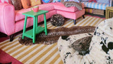 Cozy living room with pink sectional sofa, green side table, striped beige rug, and leopard print accents