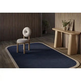 Modern interior with navy blue rug featuring cream border, minimalist wooden chair, and console table