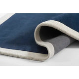 close-up of navy blue rug with cream border rolled on white surface, showing soft texture and backing