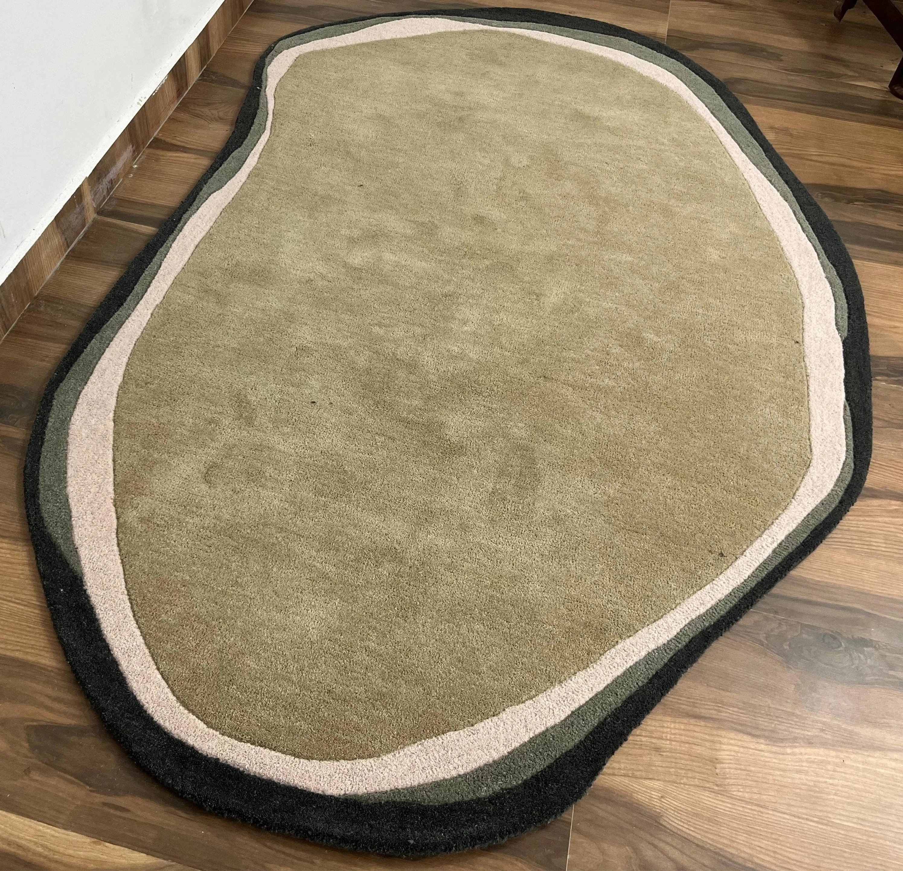 Organic shape hand-tufted wool rug in olive green with beige and black border.
