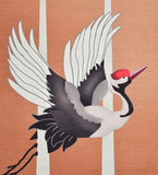 Handwoven luxury rug featuring a stylized flying crane bird with white wings and a red head on a peach background