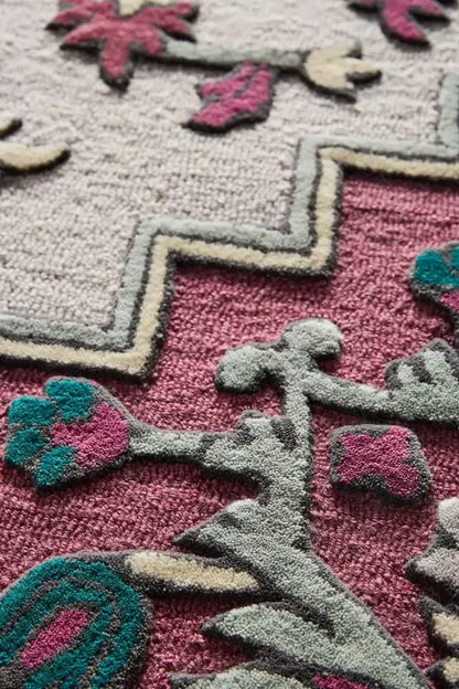 Close-up of a textured rug with geometric patterns in pink, gray, and green.