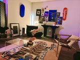 Modern living room with pink tiger motif rug, clear acrylic table, black and white chairs, and colorful artwork