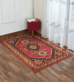 Red antique-style handwoven rug with intricate floral and geometric patterns on wooden floor by white wall and sheer curtain