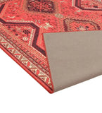Red tribal handwoven rug with geometric and floral patterns, corner flipped to show backing