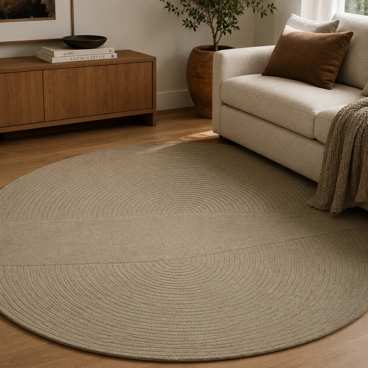 Round beige rug in a living room with a beige sofa and wooden cabinet.