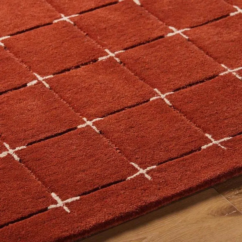 Artisanal hand-tufted grid rug in rustic red and cream tones.