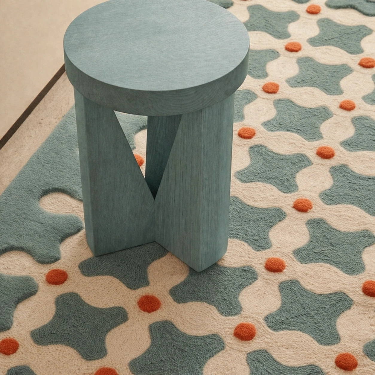 Blue stool on a patterned rug with geometric shapes and orange dots.