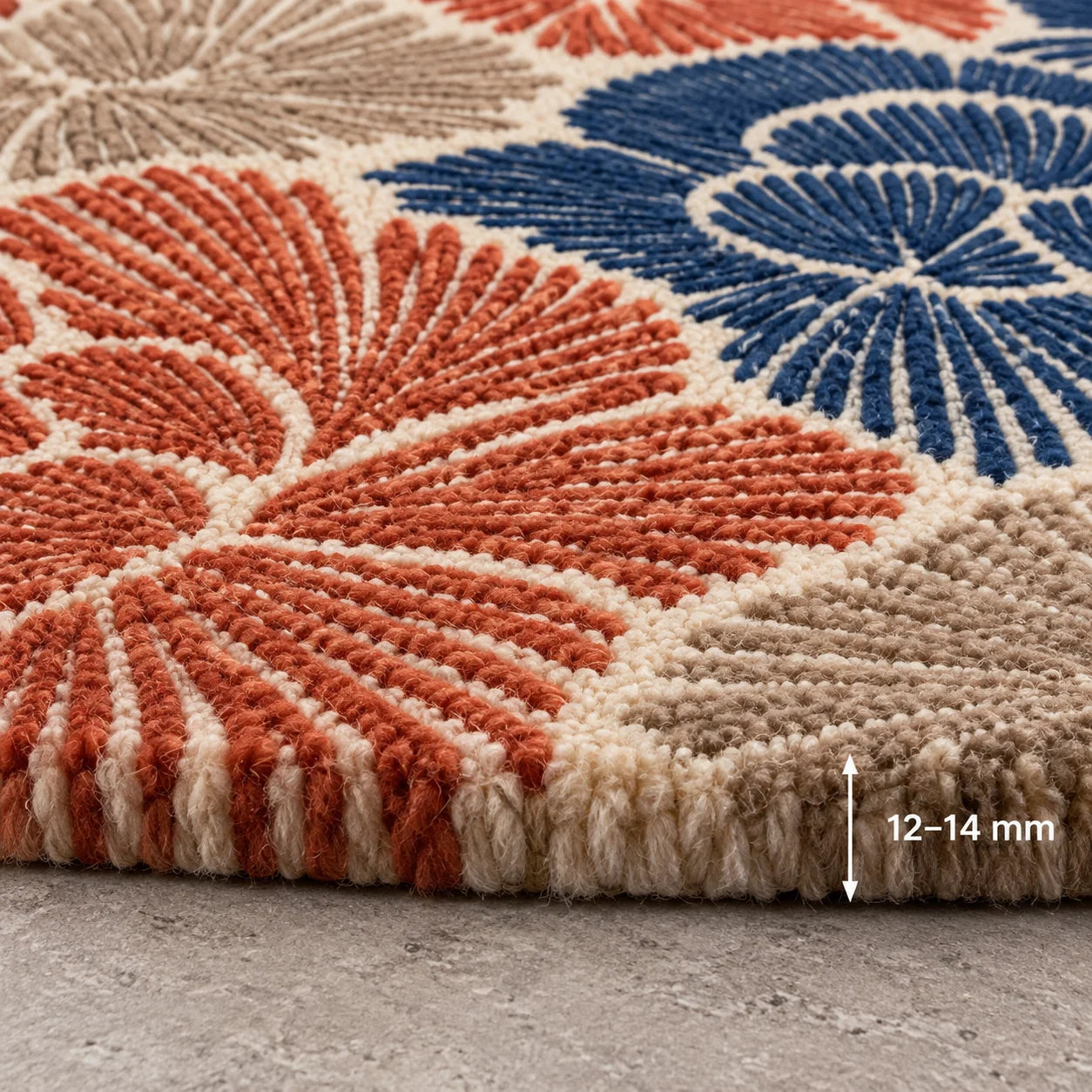 Close-up of a textured area rug with a geometric fan pattern in terracotta, navy blue, and cream, shown on a gray concrete floor with a '12-14 mm' height indicator overlay.