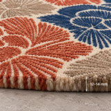 Close-up of a textured area rug with a geometric fan pattern in terracotta, navy blue, and cream, shown on a gray concrete floor with a '12-14 mm' height indicator overlay.