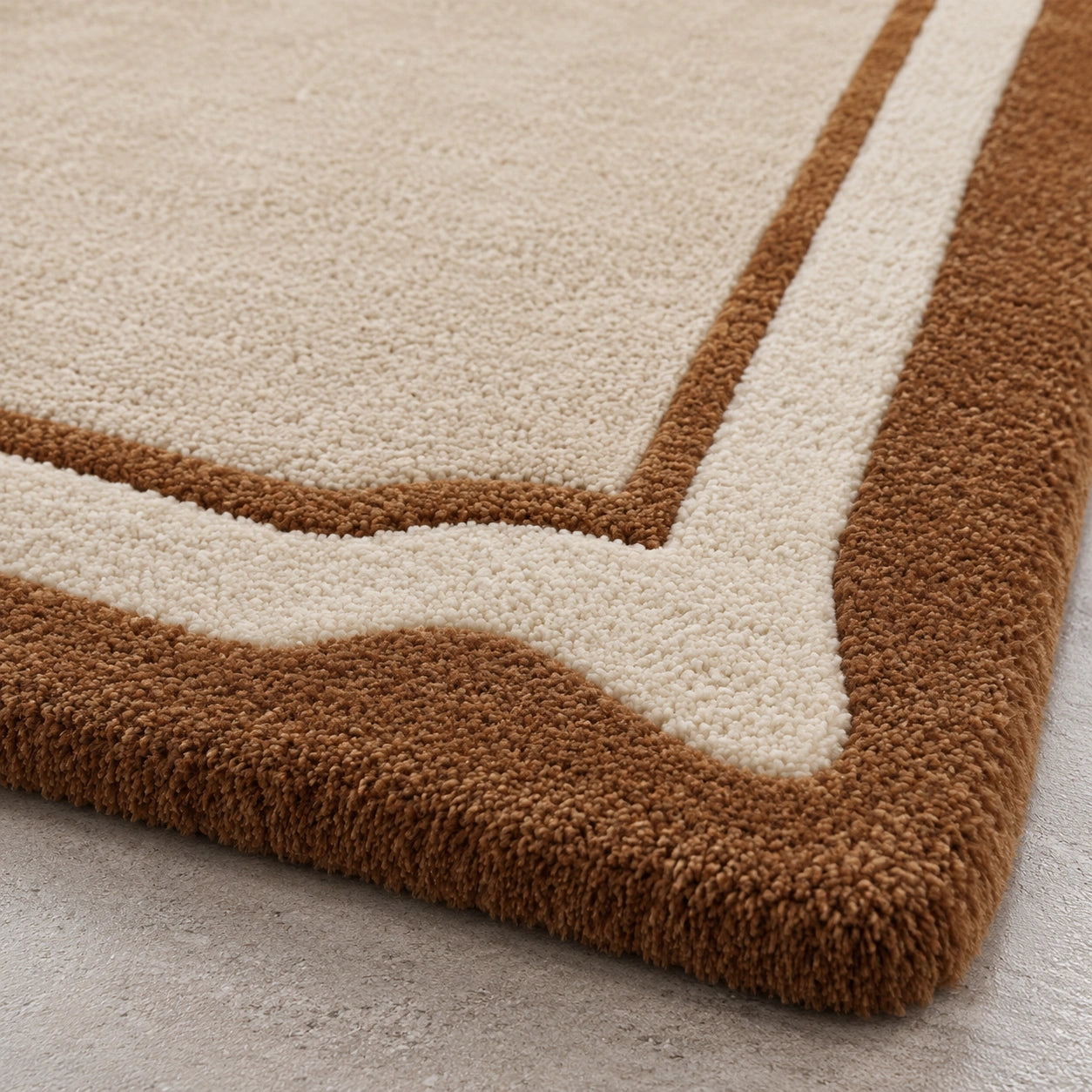 Close-up of a plush area rug corner showing a cream center field with a wavy brown border, photographed on a light neutral floor.
