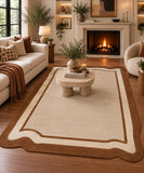 A large rectangular area rug with a cream center and brown scalloped border, styled in a warm, modern living room with a fireplace, sofa, and wooden floor.