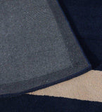 Close-up of a solid blue minimalist rug with a folded corner revealing textured grey backing