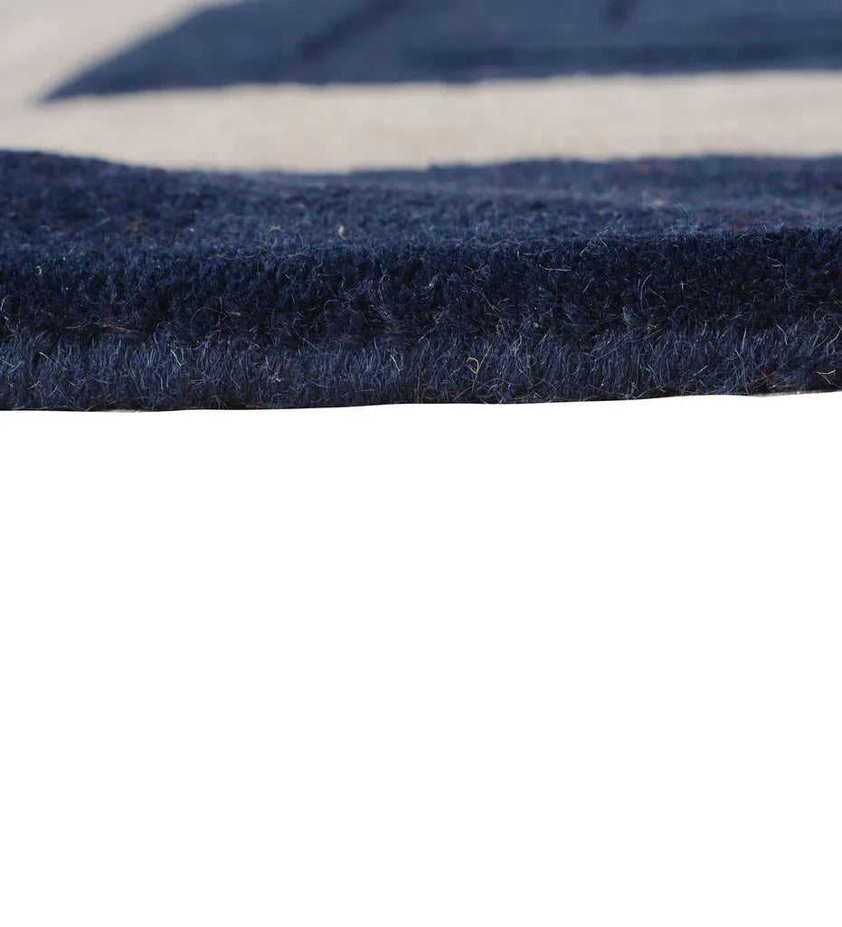 Close up and pile thickness of navy blue hand-tufted wool rug with beige rectangular border in a modern minimalist design.