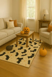Cozy living room with beige furniture, bat-themed Halloween rug, and carved pumpkins on wooden floor