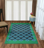 Teal and black damask style luxury handwoven rug on wooden floor in modern room with chair and patterned ottoman