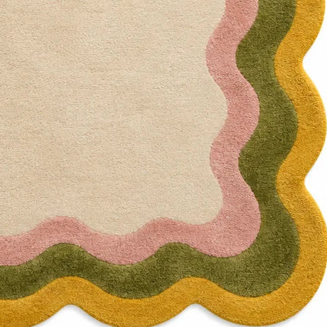 A rectangular area rug with a scalloped border featuring concentric bands of mustard yellow, olive green, dusty pink, and a warm cream center, shown flat against a white background.