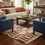 Terracotta and beige geometric area rug in a stylish living room with cream sofa, blue chairs, wood coffee table, and decorative accents