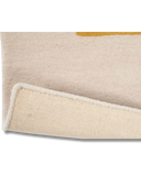 Close-up of a beige luxury handwoven rug with folded corner showing textured cotton backing and subtle mustard accent