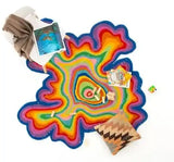 Irregular hand-tufted multicolor rug with vibrant concentric layers, styled with a beige throw, books, and a patterned pillow