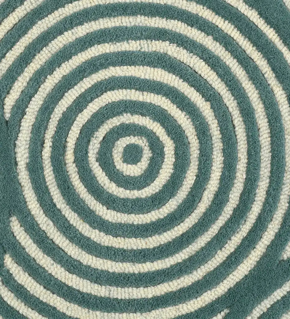 A close-up of a circular rug with concentric spiral patterns in muted teal and off-white, showing the textured looped pile of the fabric.