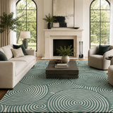 A large area rug with a teal and off-white concentric spiral pattern, styled in a bright, modern living room with a white sofa, two beige armchairs, a dark wood coffee table, and a white fireplace.