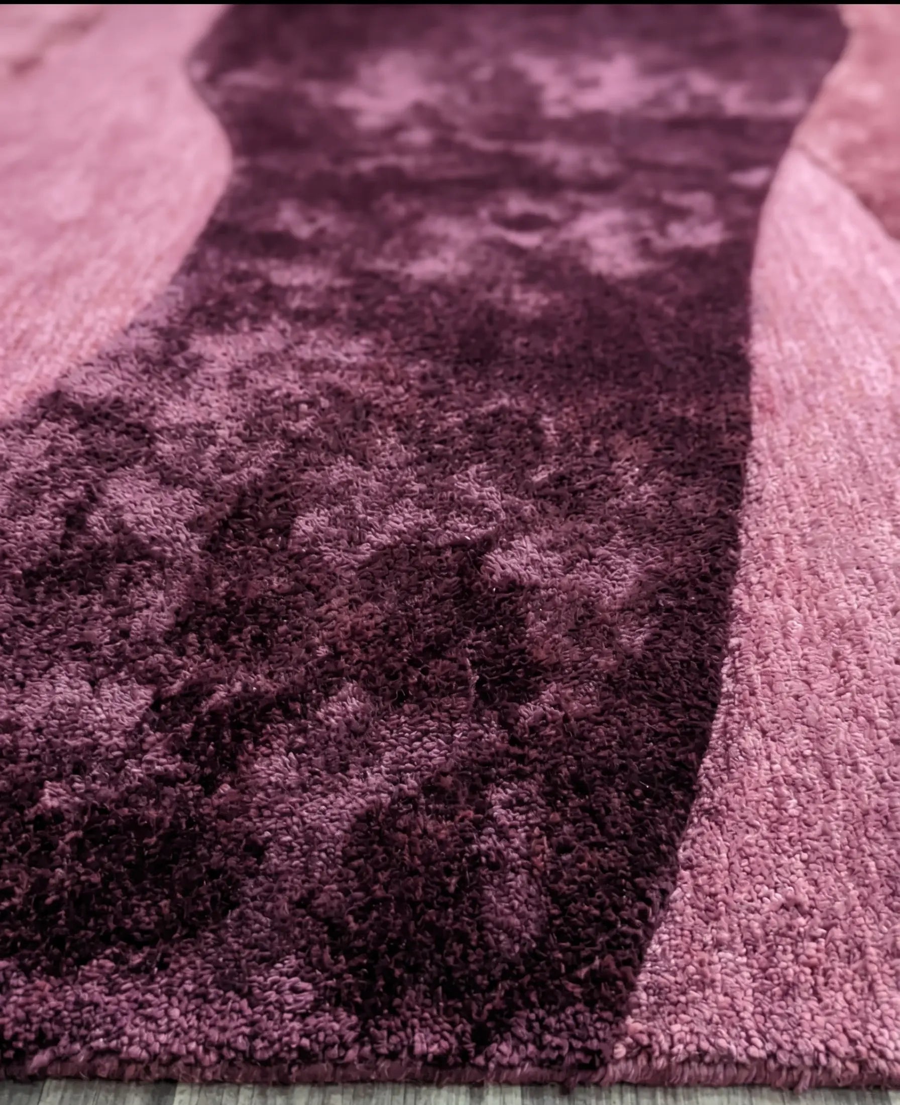 Close-up of a textured purple rug with a checkered pattern on a light wooden floor.