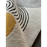 Close-up of luxury handwoven rug with beige background, black curved lines, and mustard yellow circular accent