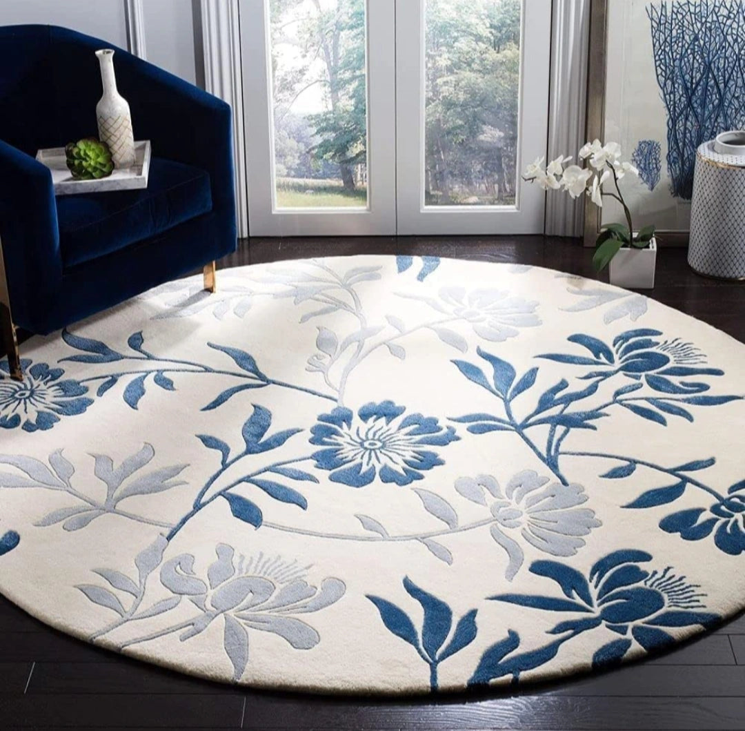 A round area rug with a blue and gray floral pattern on a cream background, styled in a modern living room setting next to a dark blue armchair.