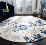 A round area rug with a blue and gray floral pattern on a cream background, styled in a modern living room setting next to a dark blue armchair.