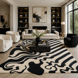 A large modern area rug with a bold black and cream abstract wavy pattern, styled in a contemporary living room with a black marble coffee table, white sofa, and black accent chairs.