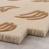 Close-up of a plush area rug with a cream base and raised tan abstract leaf-like patterns, shown on a light gray floor.