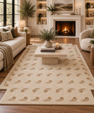 A large cream-colored area rug with a repeating tan leaf pattern, styled in a cozy, modern living room with a fireplace, sofa, and coffee table.