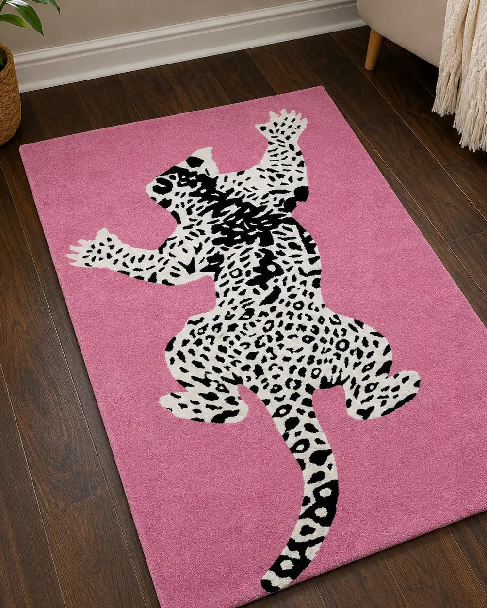 A pink rectangular area rug with a large black-and-white spotted leopard silhouette design, shown on a dark wood floor in a living room setting.
