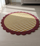 Round rug with red scalloped edge and yellow striped center on a wooden floor.