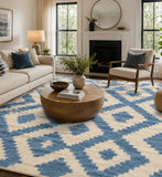 A large area rug with a blue and cream geometric diamond pattern is shown in a styled living room with a beige sofa, wooden coffee table, and fireplace.