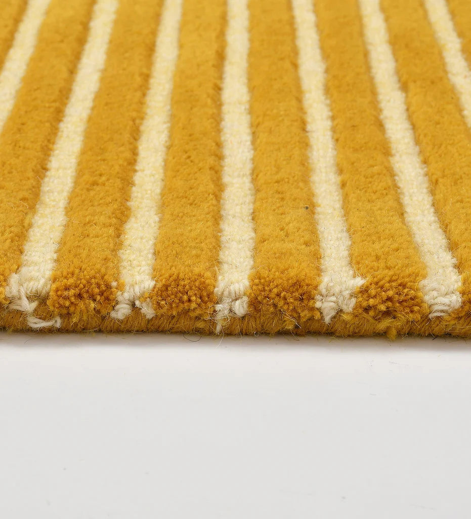 A close-up of a plush area rug with vertical mustard yellow and cream stripes, showing the textured pile and fringed edge against a plain white background.