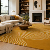 A large mustard yellow area rug with a cream geometric concentric arch pattern, styled in a modern living room with a cream sectional sofa, round wooden coffee table, and fireplace.